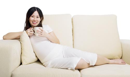 Pregnant woman drinks coffee on couch