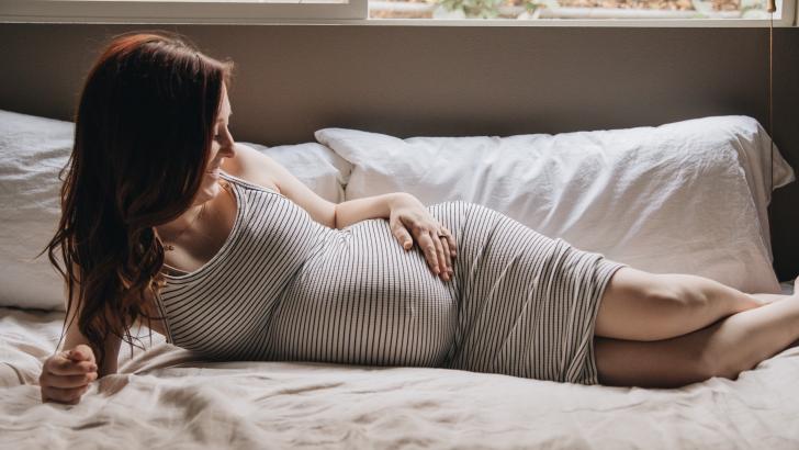 smiling pregnancy woman in striped dress resting in bed